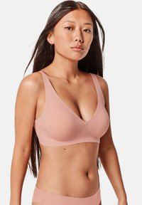 Soutien-gorge rose clair sans couture avec de larges bretelles, un décolleté en V et une texture lisse. Présente des détails élégants le long de la bande.