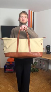 Płócienna torba podróżna z brązowymi skórzanymi akcentami, wyposażona w dwa solidne uchwyty, duży otwór oraz prostokątny kształt.