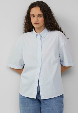 Lichtblauwe korte mouwen knoopshirt met een puntige kraag, frontplacket en opgerolde mouwen. Stof lijkt glad en lichtjes gestructureerd.