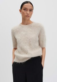 Pull léger beige à manches courtes en matière moelleuse avec un col rond et une coupe décontractée, associé à un pantalon noir.