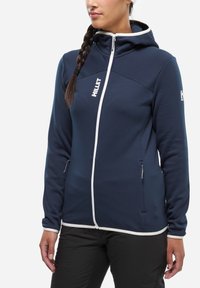 Granatowa bluza z kapturem na pełny zamek i białymi akcentami, wykonana z miękkiego, teksturowanego materiału. Posiada kaptur oraz kieszenie na zamek.