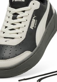 Puma CA Match sportiniai batai juodos ir pilkos odos, su tekstūruoto zomšo akcentais, perforuotu dizainu ir plokščiomis juodomis raištelėmis. Matoma guma padanga.