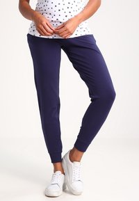 Námořnické jogger kalhoty vyrobené z měkké látky, s ribkovanými manžetami a bočními kapsami. V kombinaci s potištěným bílým tričkem a bílými teniskami.