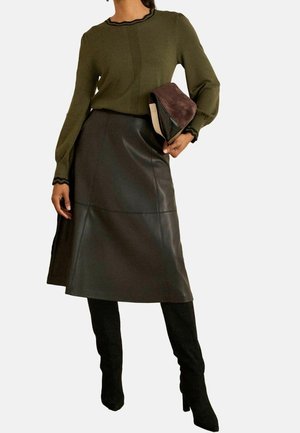 Kvinde iført en olivengrøn langærmet sweater, mørkebrun læder midi nederdel, sorte knæhøje støvler, holder en brun og beige clutch.