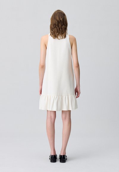 Vestido sin mangas en color crema con un dobladillo acampanado y volantes, confeccionado en una tela suave. Presenta una silueta relajada y un diseño sencillo.