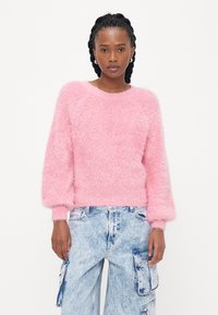 Fluffy roze trui met een ronde hals en pofmouwen, gecombineerd met lichtblauwe cargo-pantalons met zijzakken en een vervaagd textuur.