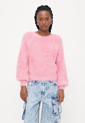 Fluffy roze trui met een ronde hals en pofmouwen, gecombineerd met lichtblauwe cargo-pantalons met zijzakken en een vervaagd textuur.