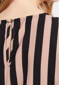 Blusa con rayas verticales en negro y rosa empolvado, hecha de una tela texturizada. Una abertura en forma de llave en la parte posterior se cierra con un pequeño botón.