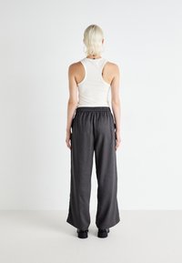 Witte geribbelde tanktop met een ronde hals, gecombineerd met losse, donkergrijze wijde broekspijpen met een elastische tailleband. Zwarte schoenen.
