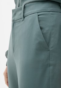 Svetle zelené kalhoty hladké textury, s boční kapsou a poutky na opasek. Design zahrnuje úzký pas a přizpůsobenou siluetu.