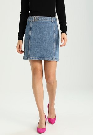 Jupe en jean mini avec passants de ceinture, tissu bleu, forme en A, ourlet effiloché, assortie à des chaussures à talons hauts roses et un haut noir à manches longues.