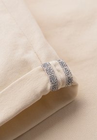 Gros plan sur un poignet en tissu beige avec une couture décorative noire et blanche à motif sur le bord plié.