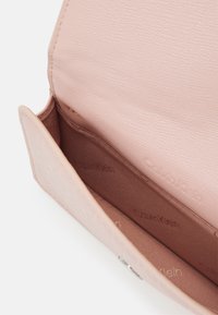 Lyserød Calvin Klein pung med tekstureret yderside, der har en glat indvendig foring, brun logo-tryk og en knaplukning.