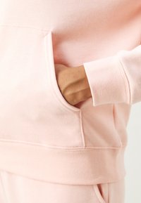Main insérée dans la poche avant d'un sweat-shirt rose clair avec un pantalon assorti visible en bas.
