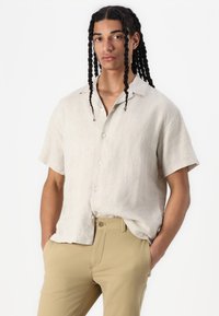 Lichtbeige linnen shirt met korte mouwen en een relaxte pasvorm, voorzien van een knoopsluiting aan de voorkant en een natuurlijke textuur. Gecombineerd met lichtkhaki broek.