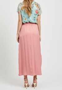 Blouse légère à motifs floraux de couleur bleu clair avec des manches courtes, assortie à une longue jupe rose fluide. La jupe possède une taille élastique.