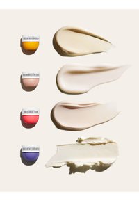 Vier kleine, meerkleurige crèmepotjes met labels, elk naast een bijbehorende gladde crèmelaag op een lichte achtergrond.