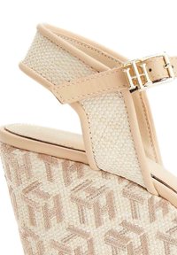 Sandalo con zeppa che presenta una tomaia intrecciata beige, cinturino in pelle con fibbia e design texturizzato. Piattaforma in sughero elevata con un delicato motivo a logo.