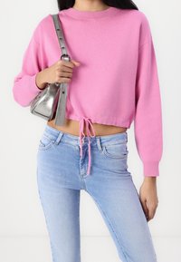 Rosa kortärmad tröja med rund halsringning och dragsko i nederkanten, i kombination med ljusblå jeans. Tröjan har långa ärmar och en texturerad finish.