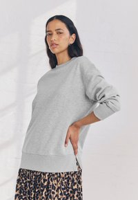 Pilka medvilnės mišinio džemperis su apvalia iškirpte, ilgomis rankovėmis ir šoninėmis skeltukėmis, derinamas su leopardų rašto raštuota sijonu.