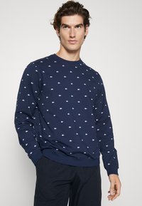 Navy blue sweatshirt with long sleeves, round neck, featuring small white logo patterns throughout. Comfortable fabric with ribbed cuffs and hem.