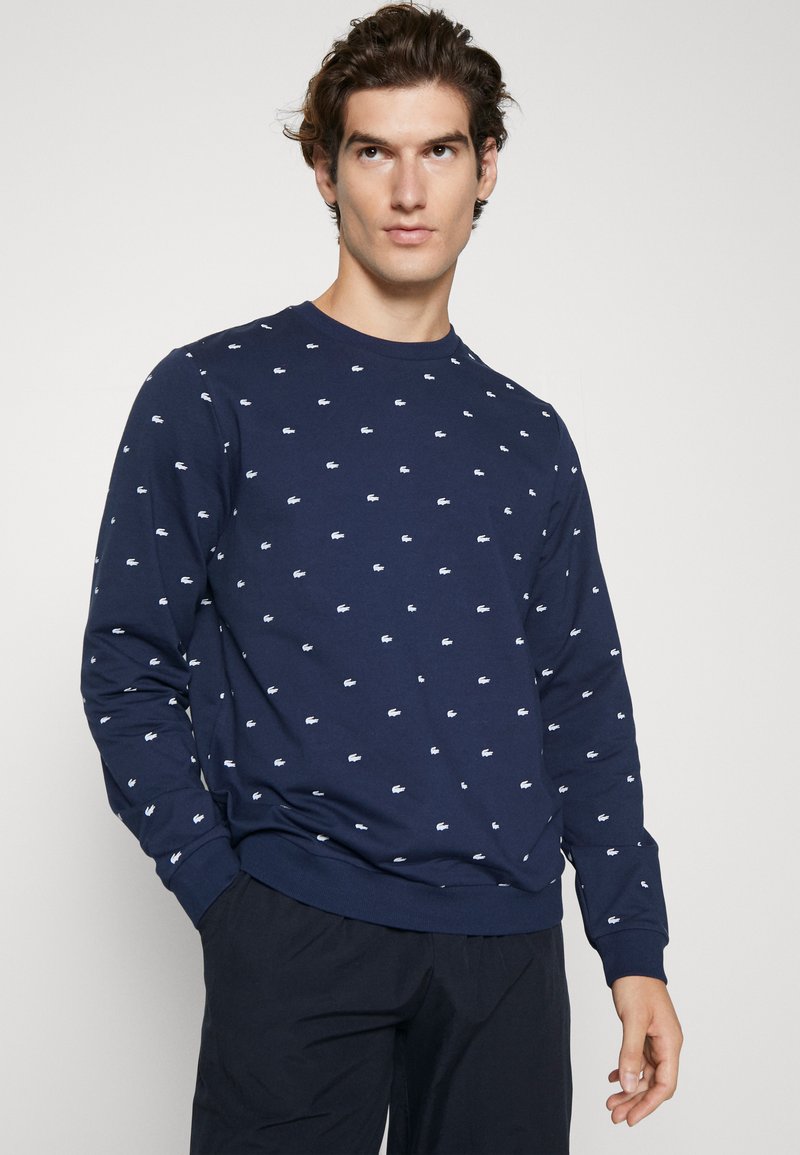 Marineblaue Sweatshirt mit langen Ärmeln, Rundhalsausschnitt, das mit kleinen weißen Logo-Mustern durchzogen ist. Bequemes Material mit gerippten Bündchen und Saum.