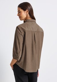 Chemise légère marron à boutons avec un col, des manches retroussables et un détail de pli à l'arrière. Texture lisse et coupe décontractée.
