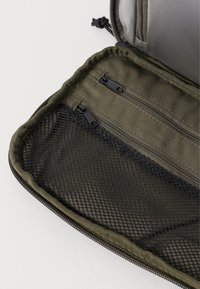 Pochette verde oliva aperta per mostrare due tasche in tessuto con zip e una tasca in rete nera con zip all'interno.