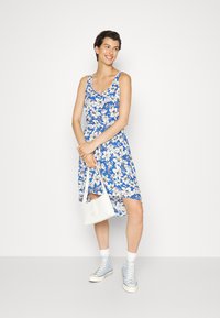 Vestido floral em tecido azul e branco, sem mangas, com decote arredondado, combinado com uma bolsa branca e ténis azul claro.