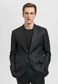 Schwarzer maßgeschneiderter Blazer mit einem subtilen Schimmer, einreihigem Design, Reverskragen und Fronttaschen, kombiniert mit einem dunklen Rundhalshemd.