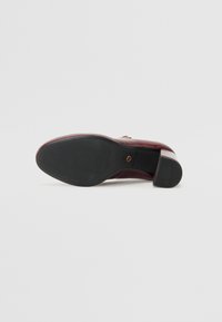 Chaussure en cuir bordeaux avec une tige texturée, un petit talon et une semelle en caoutchouc noir présentant un motif strié pour une meilleure adhérence.