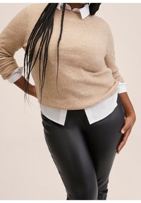 Krémový pletený svetr překrytý bílou košilí s límečkem, spárovaný s černými koženými kalhotami. Svetr má volný střih a žebrované rukávy.