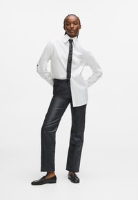 Balta krekla ar pogām un melnu kaklasaiti, apvienojot ar spīdīgām melnām taisnām biksēm un melniem loaferiem, ar mūsdienīgu un elegantu dizainu.