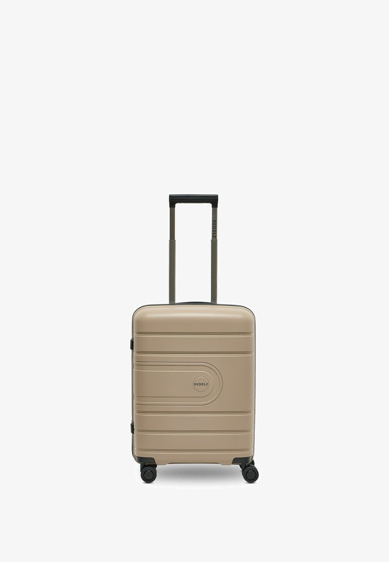 Valise rigide en plastique beige avec une surface texturée, logo central, poignée télescopique et quatre roulettes multidirectionnelles.