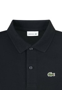 Czarna polo z teksturowanej tkaniny, z dwu guziczkową plisą, żebrowanym kołnierzykiem i zielonym logo krokodyla Lacoste na piersi.