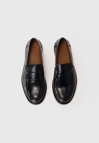Black leather loafers feature a smooth texture, rounded toe, and decorative stitched accents. The insoles are brown leather, enhancing comfort.