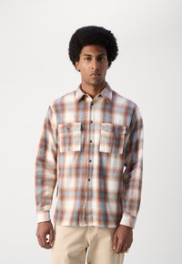 Plaid flannel shirt in cream, orange, and blue. Features two chest pockets and button front. Long sleeves with cuffed wrists.