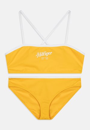 Geel bikini set met een bandeau-top met witte bies en gekruiste bandjes, gecombineerd met bijpassende low-rise onderbroekjes. Katoenachtige textuur.