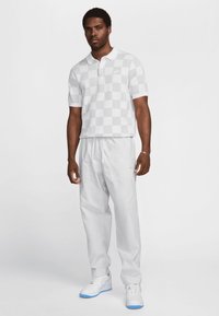 Camisa polo branca de xadrez, de mangas curtas, e calças brancas com cordão. O calçado apresenta detalhes em branco e azul claro.
