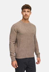 Brun strikket sweater med rund hals, ribbede manchetter og kant. Lavet af et blødt materiale, der sidder tæt til kroppen.