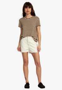 Randig brun och vit T-shirt med rund halsringning, kombinerad med högmidjade vita denimshorts. Svarta skor fulländar outfiten.