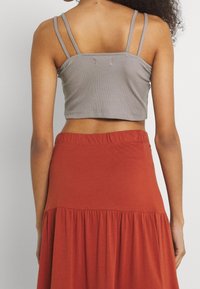 Šedý žebrovaný crop top s tenkými ramínky, který je spárován s sukní v odstínu rezavé barvy s nařaseným, rozšířeným spodním okrajem. Měkké, lehké materiály.