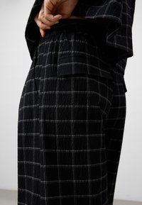 Zwart met patroon broek van een gestructureerde stof met een wit geruit ontwerp, elastische tailleband en een zijzakdetail.