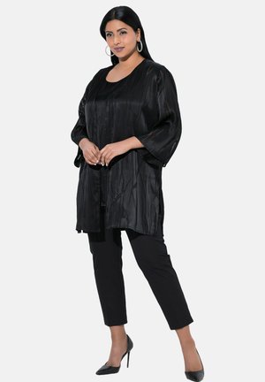 Zwarte zijden kimono-stijl top met een relaxed fit, ellebooglange mouwen en subtiele textuurpatronen, gecombineerd met zwarte slim-fit broeken en hakken.