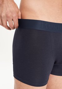 Boxer shorts di un blu navy scuro realizzati in tessuto morbido. Presentano un'ampia vita elastica con testo in rilievo e un design aderente per il comfort.