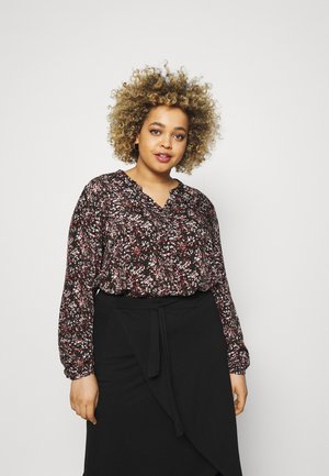 Blouse noire à motifs floraux avec des fleurs rouges et blanches, décolleté en V, manches longues et coupe ample, assortie à une jupe portefeuille noire.