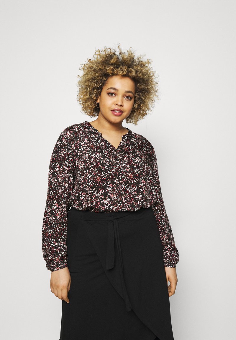 Blouse noire à motifs floraux avec des fleurs rouges et blanches, décolleté en V, manches longues et coupe ample, assortie à une jupe portefeuille noire.
