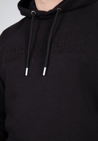 Felpa con cappuccio nera caratterizzata da testo inciso "GORILLA WEAR UNITED STATES OF AMERICA." Cordini neri con punte in argento. Tessuto morbido.