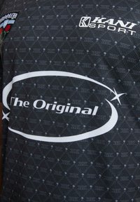Juodas sportinis marškinėliai, turintys deimantų raštą, baltu spalva užrašas "The Original" ir logotipas viršutiniame kairiajame kampe. Medžiaga yra tekstūruota.