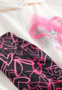 Hooded sweatshirt with a cream body, featuring pink heart designs and black fabric with pink abstract patterns. Soft texture throughout.